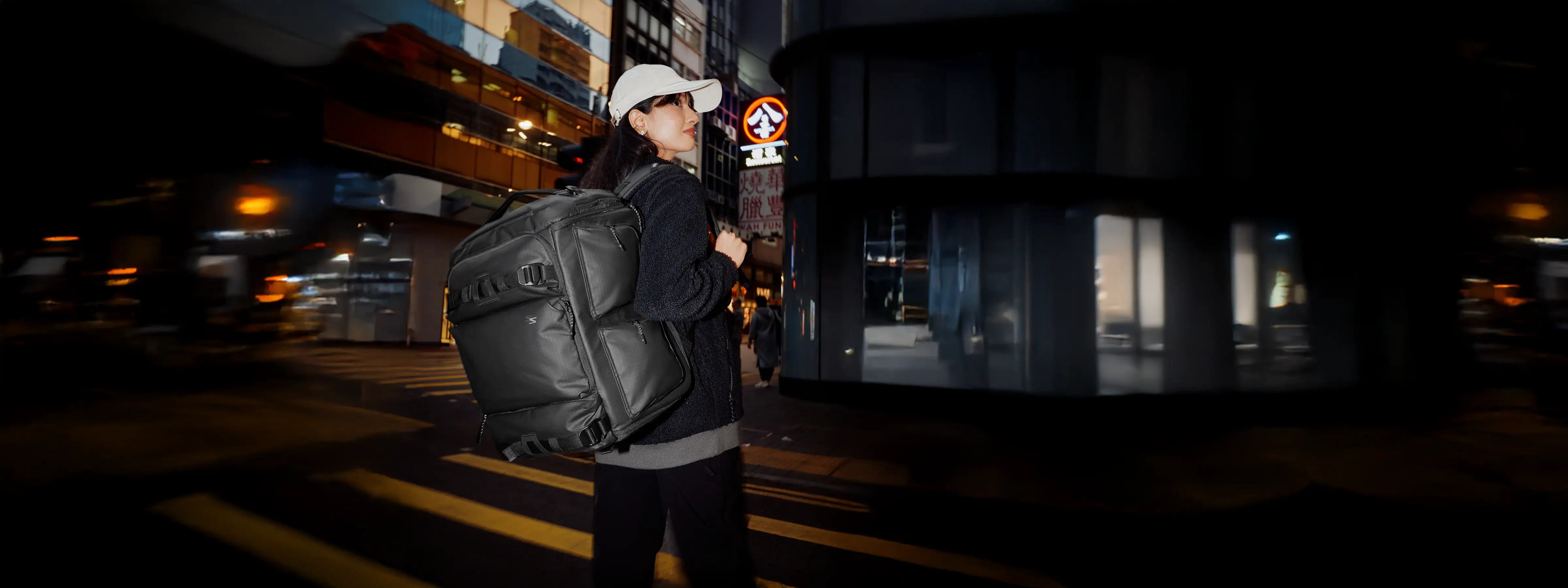 Person with a large black backpack crossing a street at night.