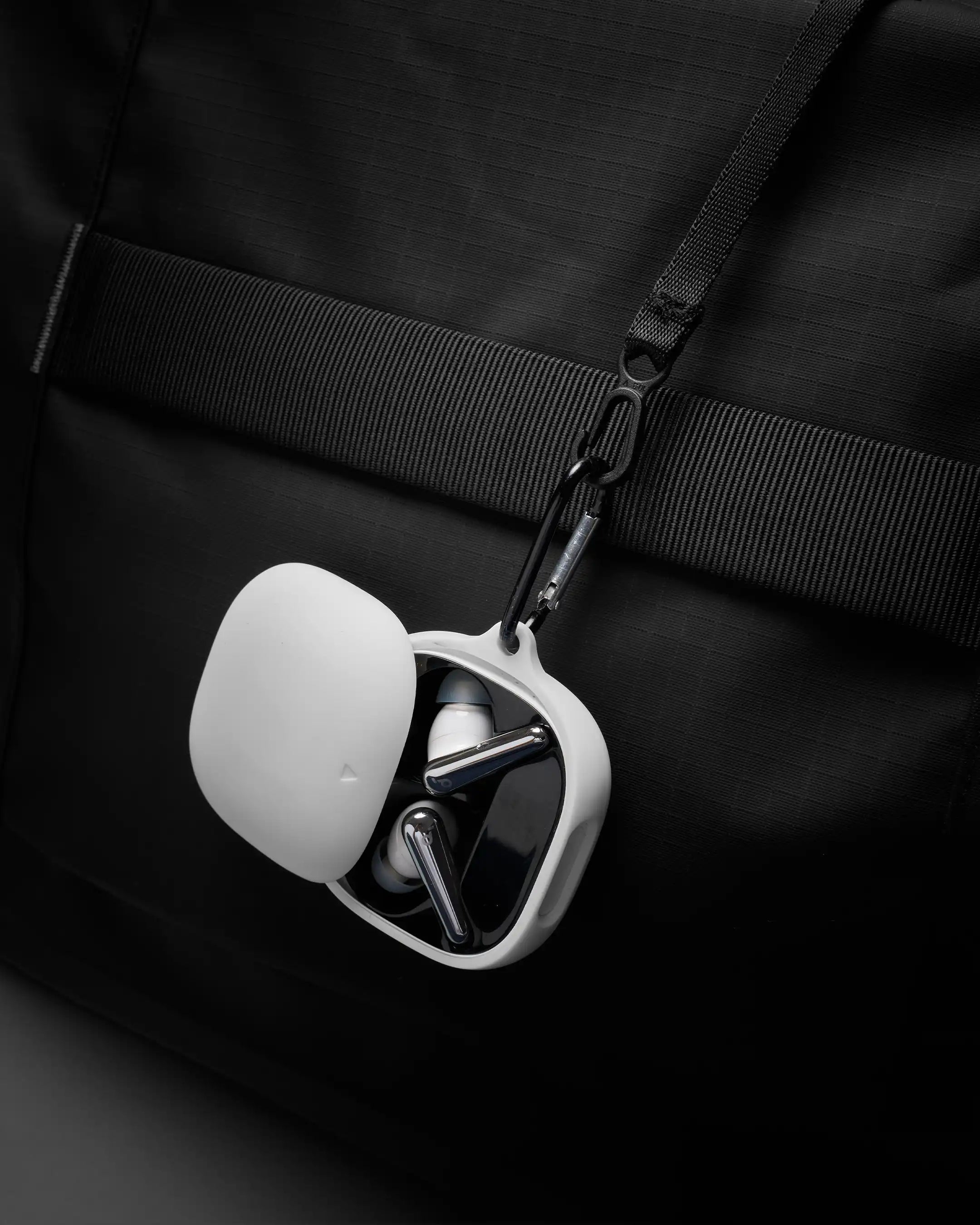 White earbud case with earbuds hanging from a black strap on a black background
