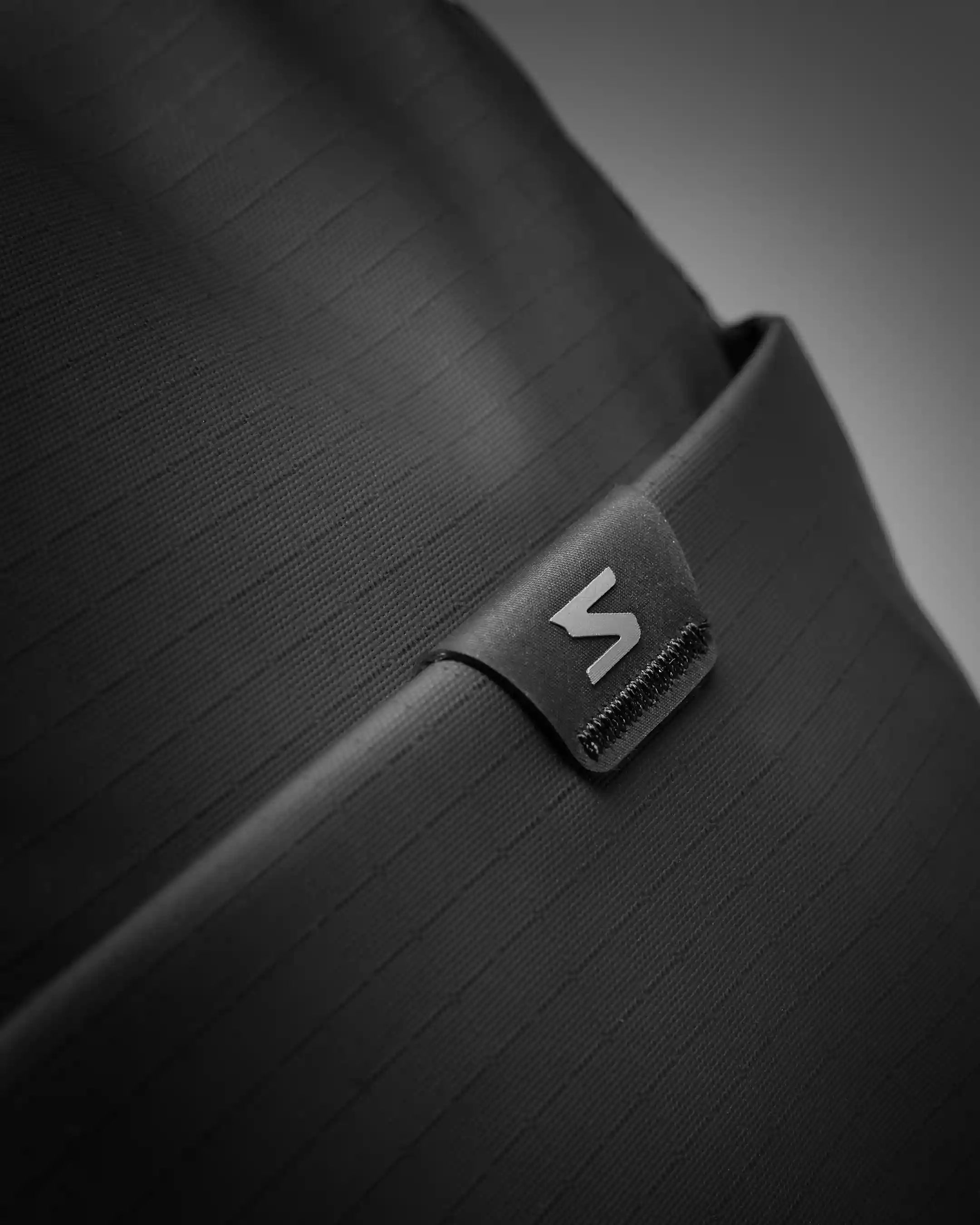 Close-up of a black bag with a brand logo on a gray background