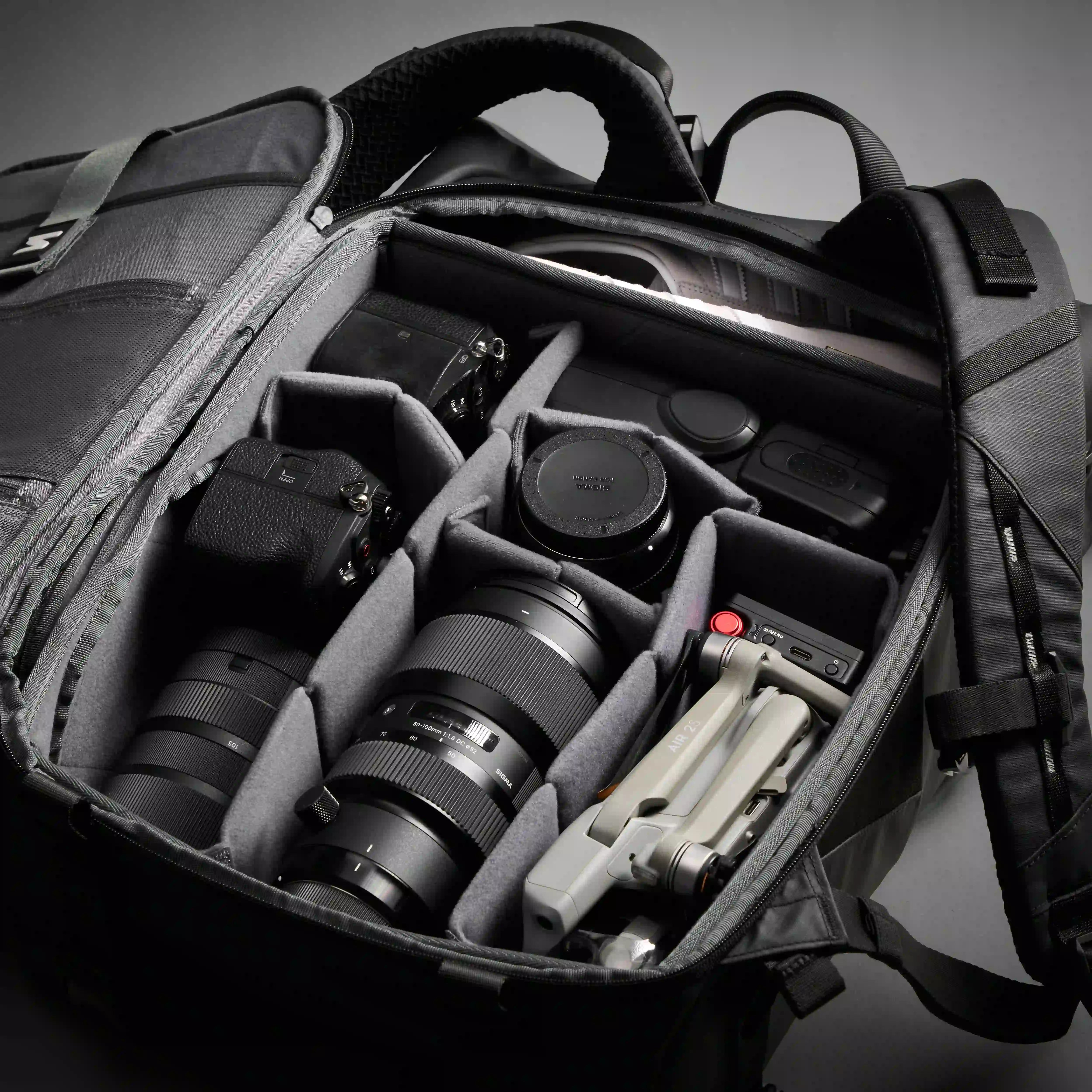 Camera bag with camera equipment including lenses and a tripod on a gray background