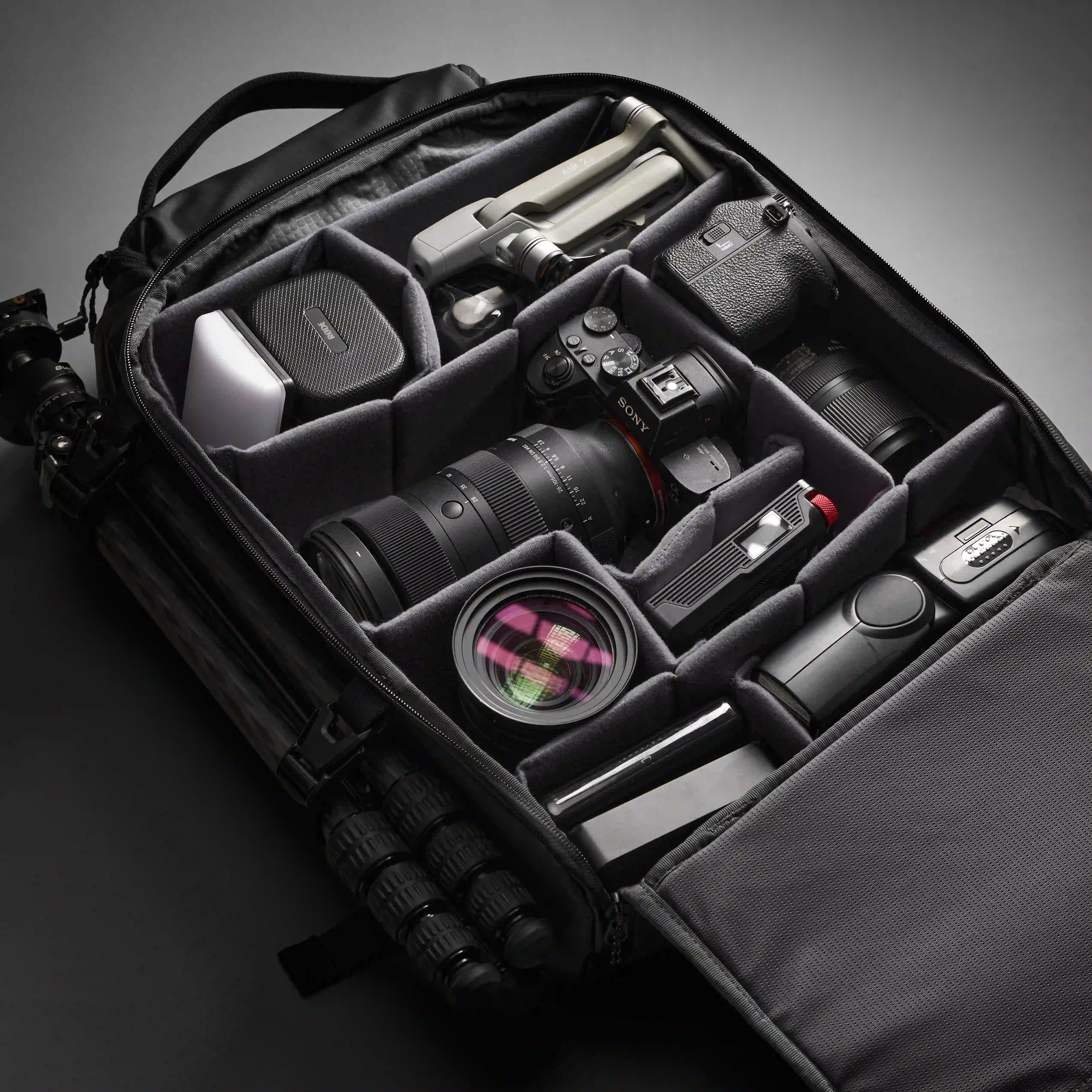 Camera equipment including a camera, lens, and accessories neatly arranged inside a black travel bag on a dark background.