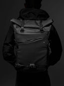 Person wearing a black rolltop backpack against a dark background