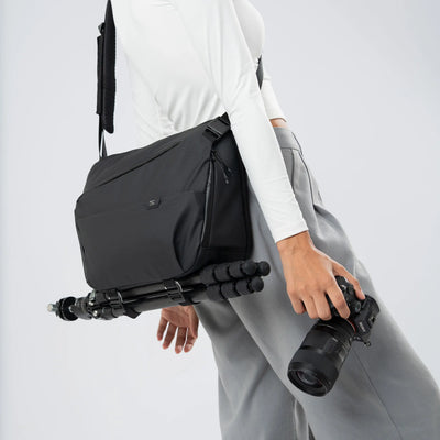 Person holding a black camera bag with a camera and tripod on a white background
