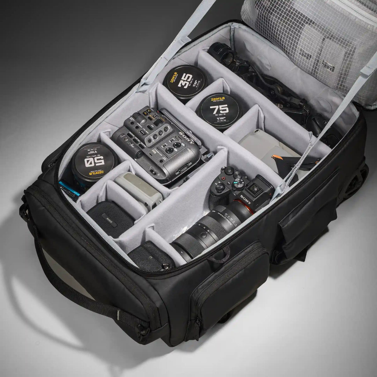An open black camera gear organizer bag filled with photography equipment, including lenses, camera bodies, and audio gear, shown on a clean light gray studio background.