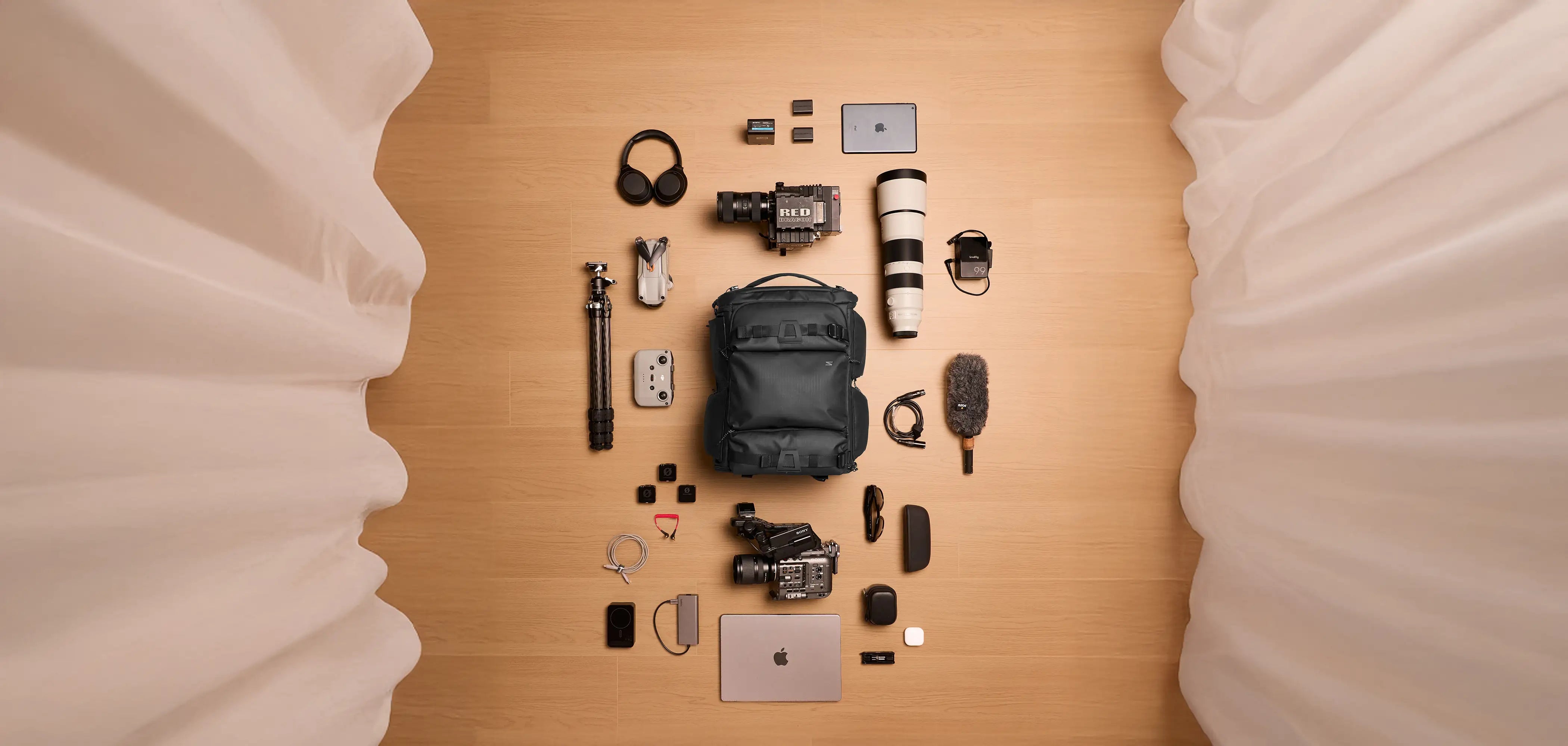 Collection of photography and videography equipment on a wooden surface with soft white curtains.