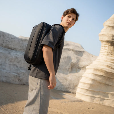 Person with a black backpack standing in a desert landscape with rock formations.