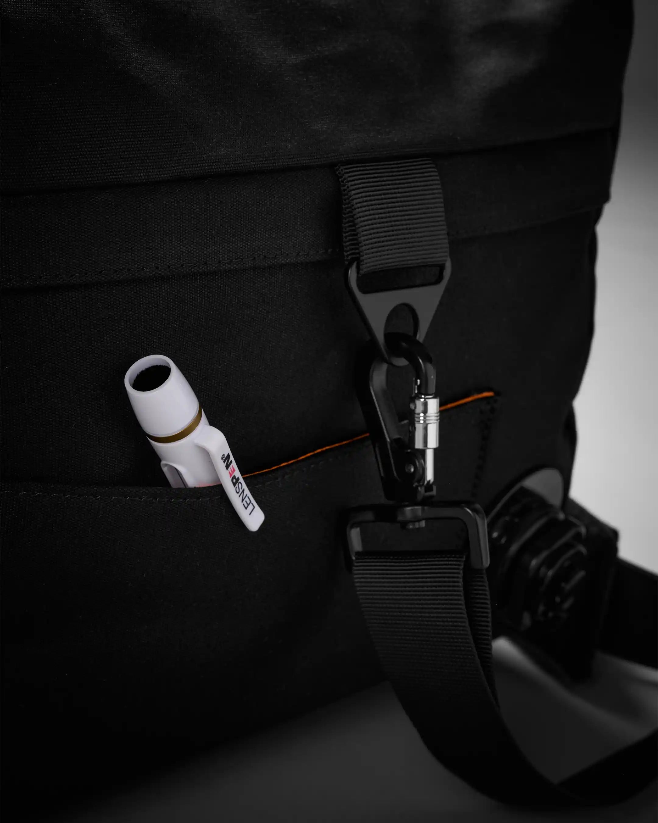 Black backpack with a strap and earbuds attached, on a dark background