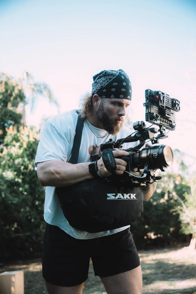 Person outdoors using a professional camera rig supported by a Sakk Gear camera bag.