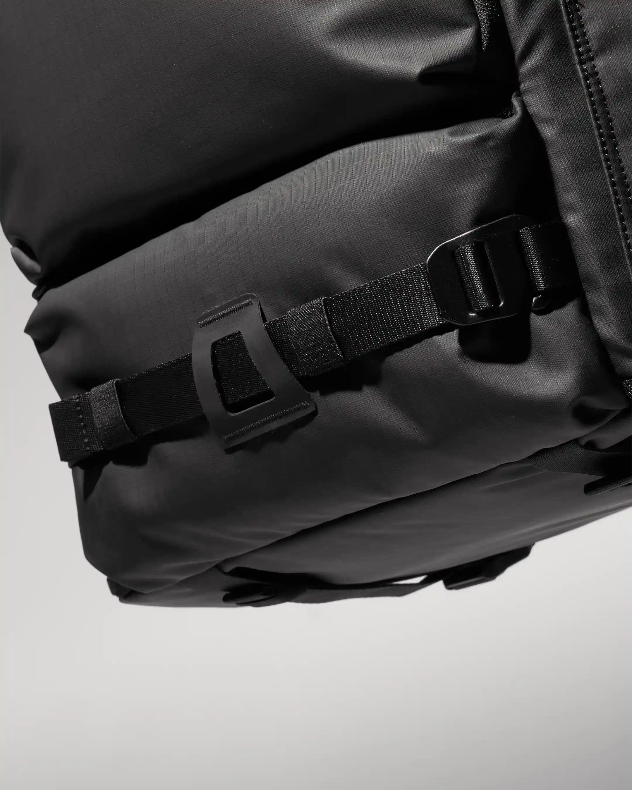 Close-up of a black backpack with visible zippers and buckles on a light gray background