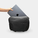 Person placing a laptop into a black backpack on a light gray background