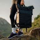 Person holding a black backpack in a mountainous landscape