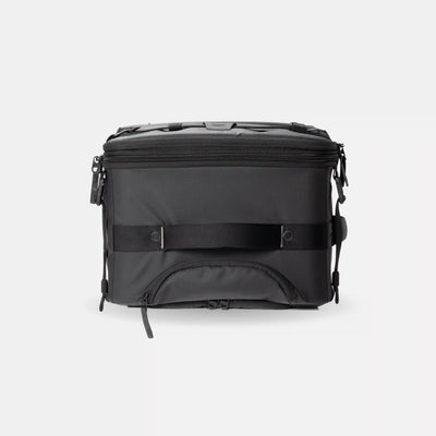 A black soft-sided cooler bag with a front zipper pocket, a horizontal compression strap, and top carry handles, shown against a light gray background.