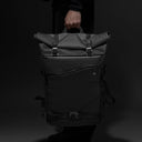 Person holding a black backpack against a dark background