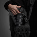 Person holding a camera with a Sony lens, with a backpack in the background