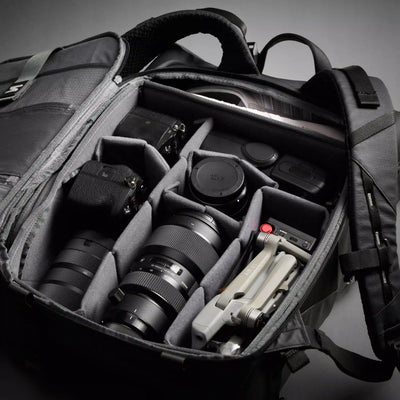 Camera bag with camera equipment including lenses and a tripod on a gray background
