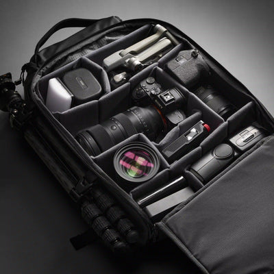 Camera equipment including a camera, lens, and accessories neatly arranged inside a black travel bag on a dark background.
