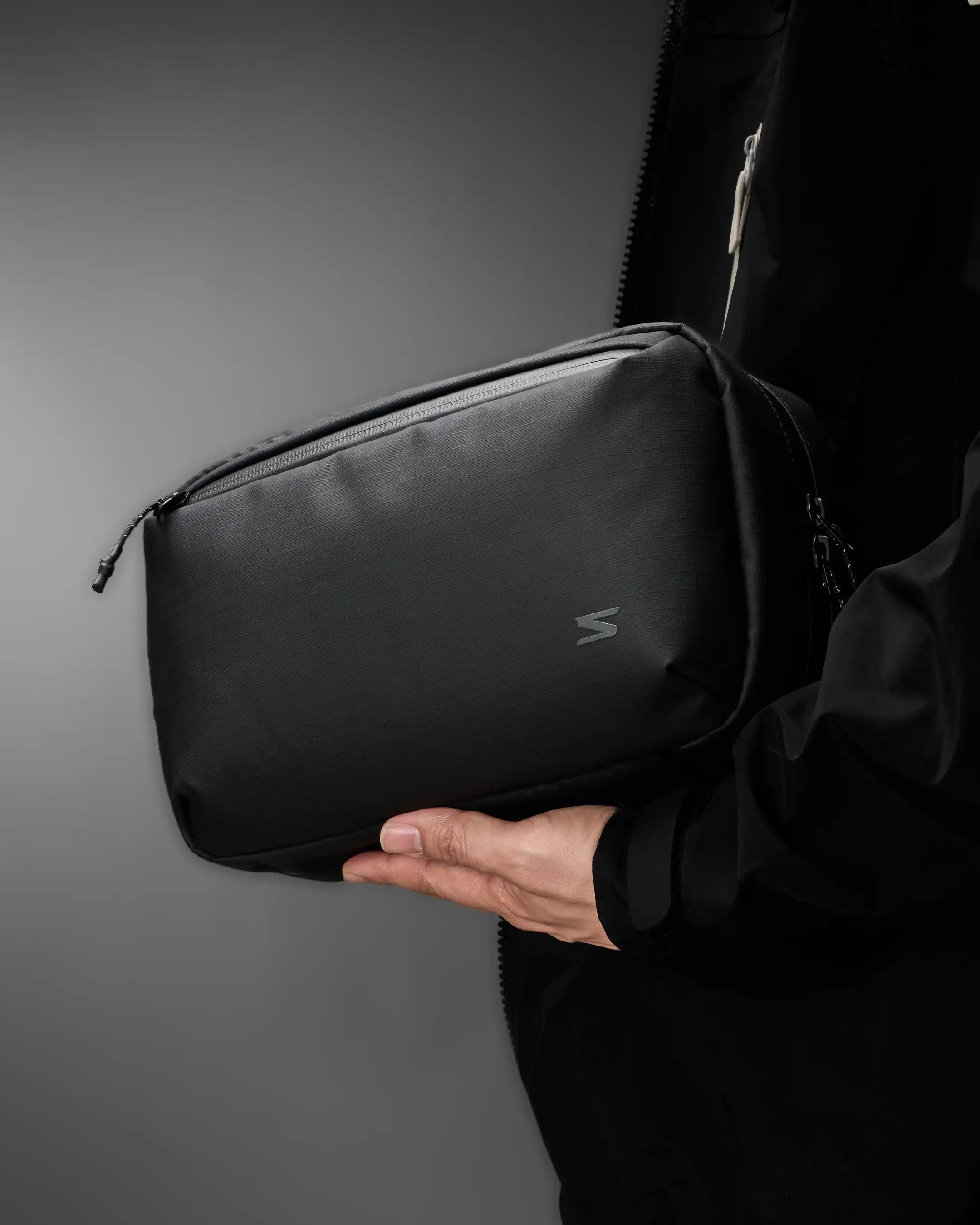 Person holding a black bag with a brand logo against a gray background