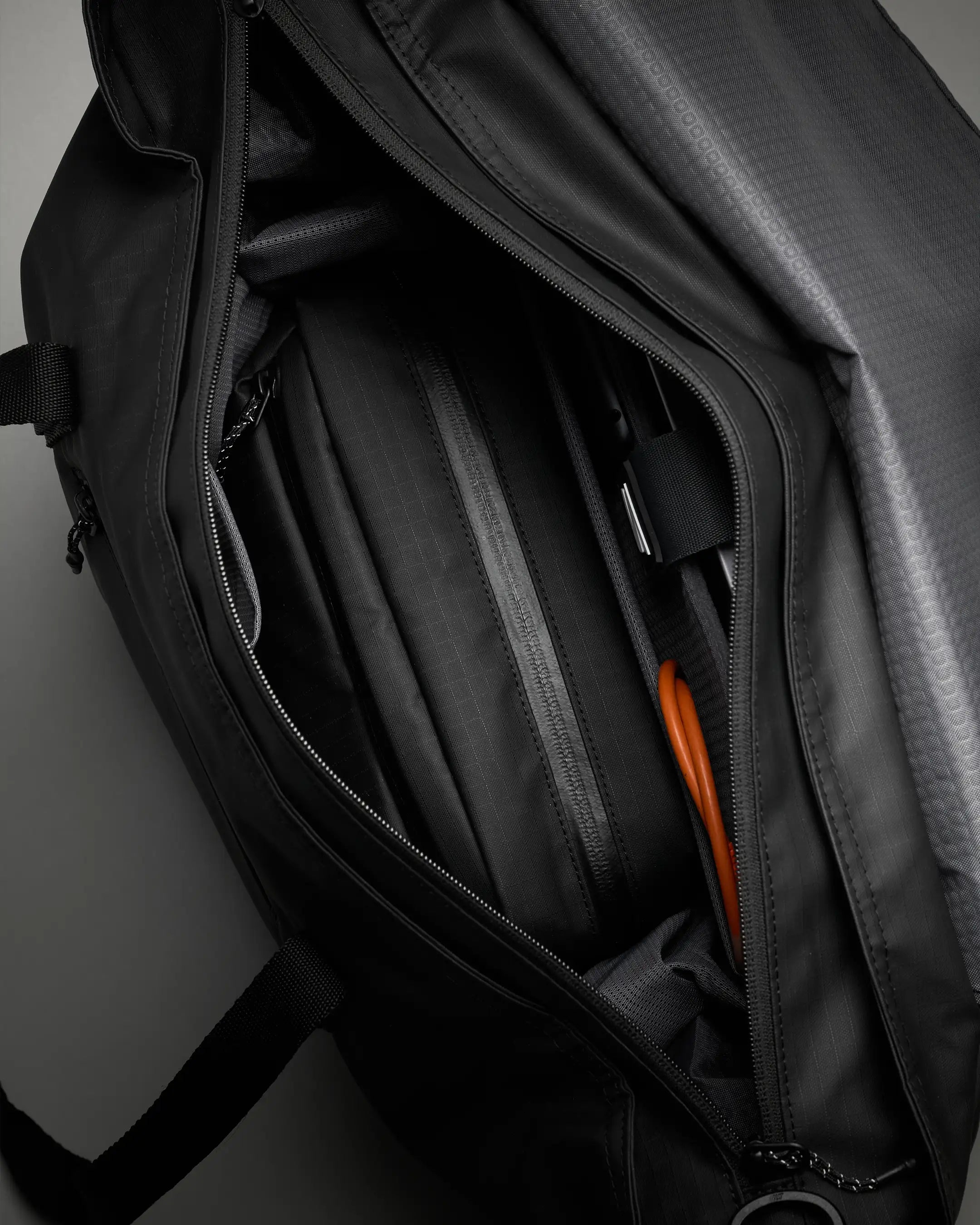 Black backpack with orange zipper partially open on a dark background