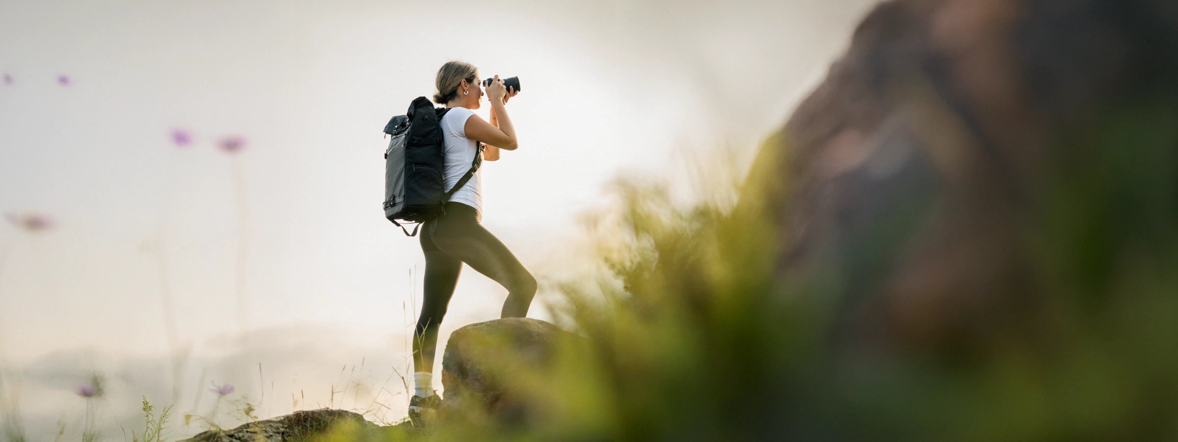 Woman with a camera backpack using binoculars on a mountain top