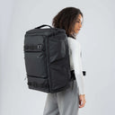 Person wearing a large black backpack on a plain background